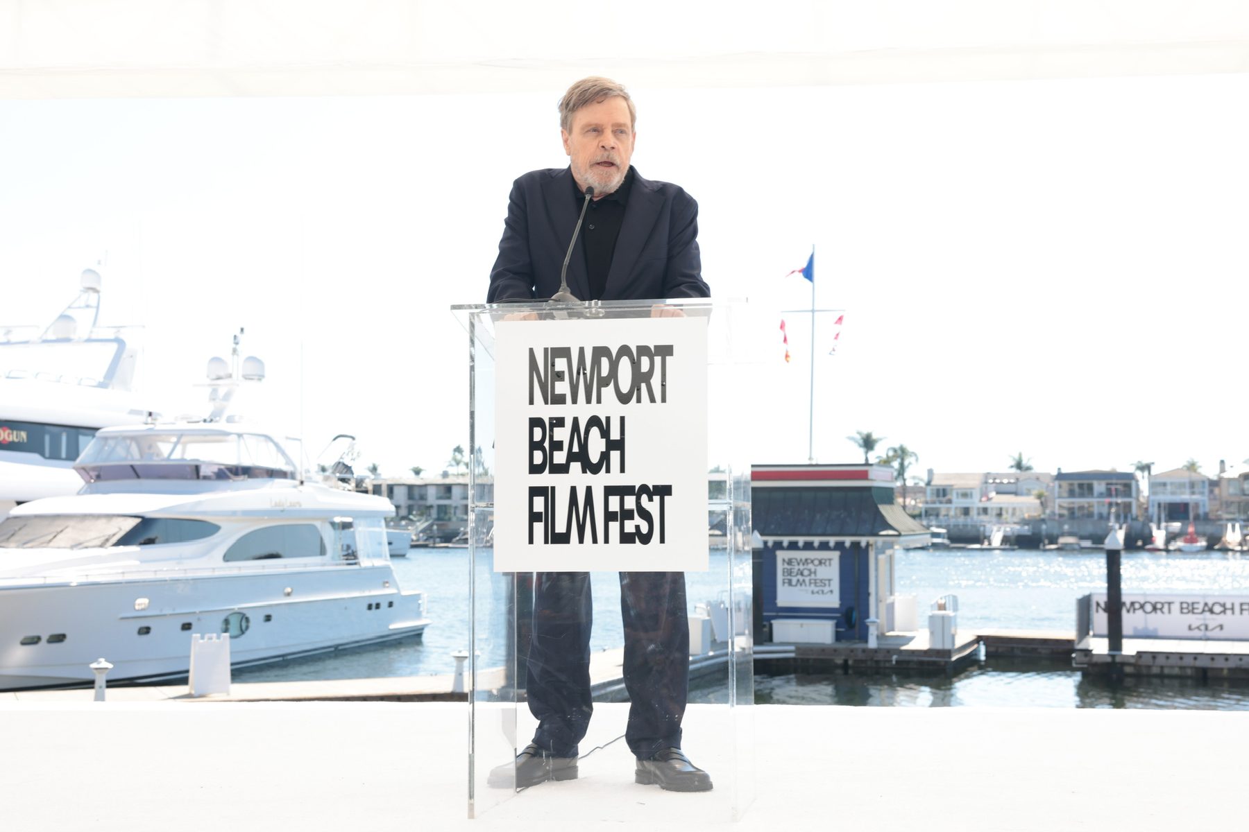 Mark Hamill speaking at a film festival lectern by the water